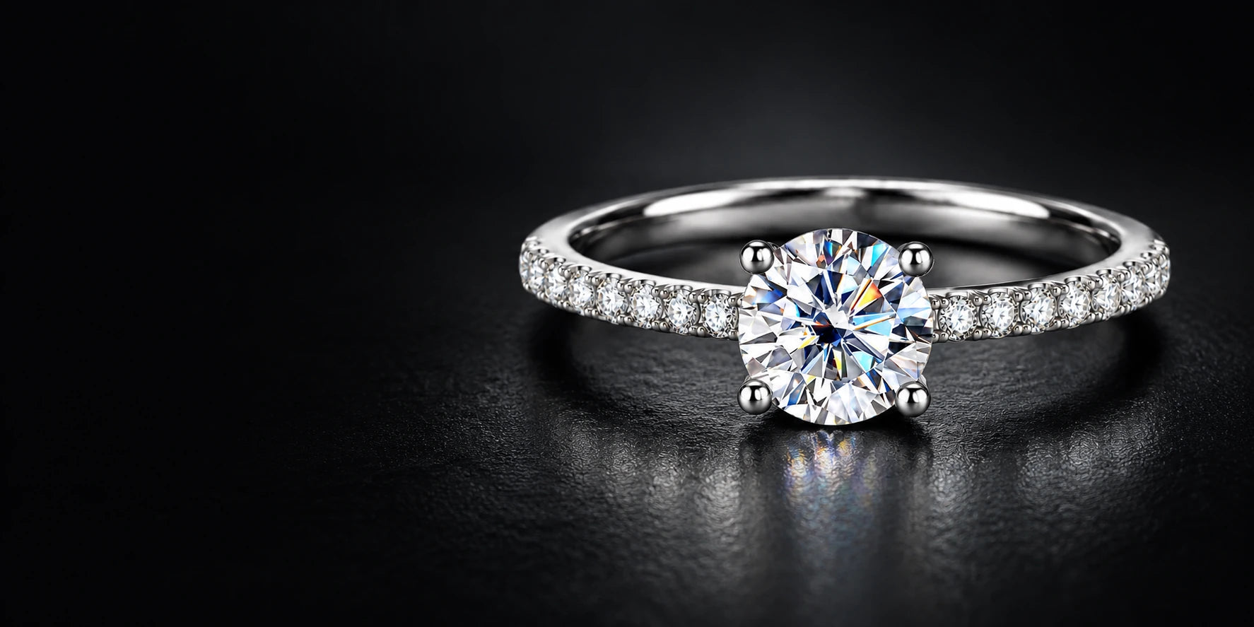 Round moissanite ring with four prongs and pavé accents on a dark surface